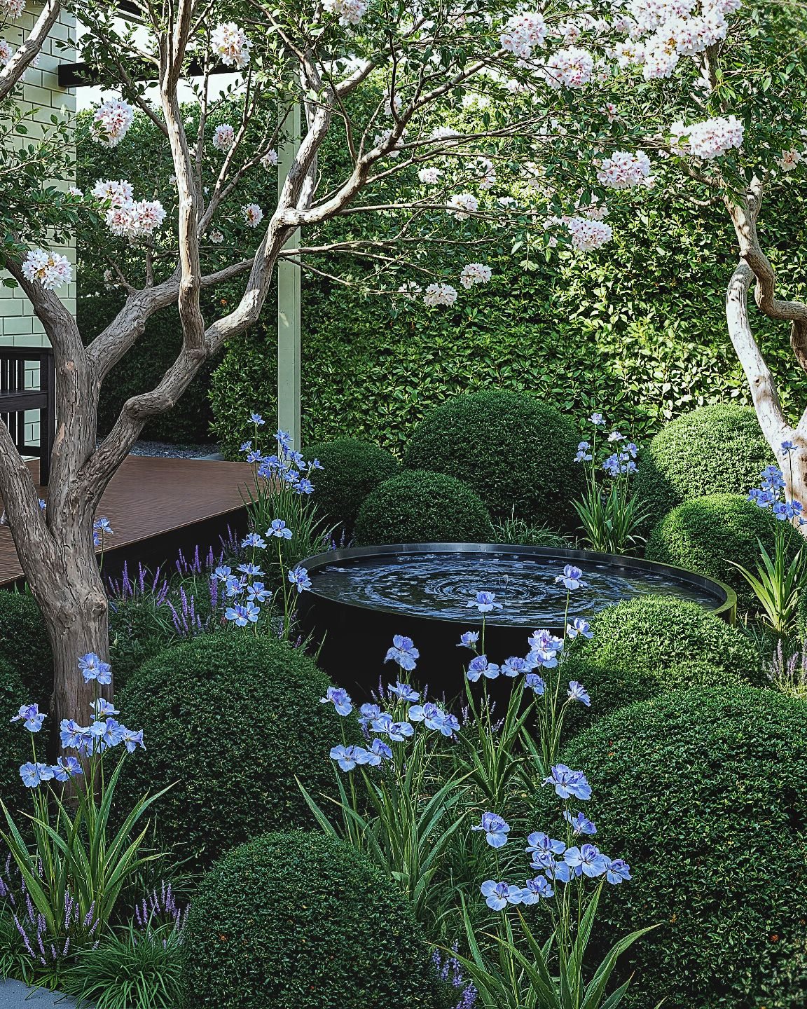 Circular water feature among flowering plants and clipped shrubs